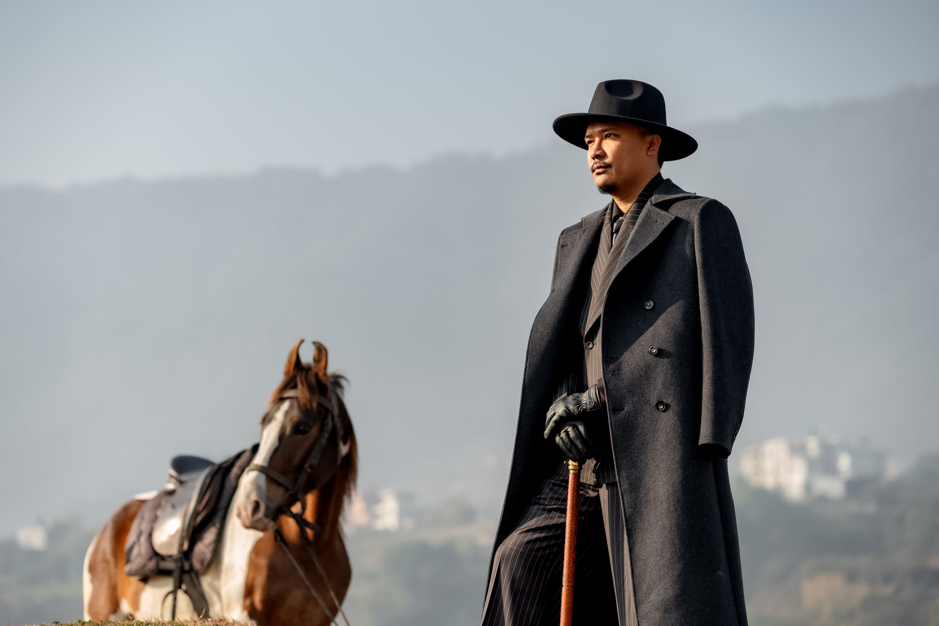 A tailored gentleman in a long overcoat standing beside a horse, The Suit Studio, Kathmandu